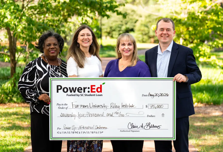 Executives pose outside holding ceremonial big check