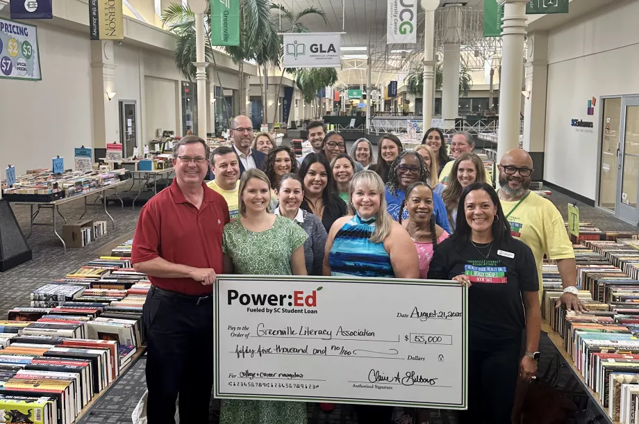 Executives pose with ceremonial big check surrounded by books