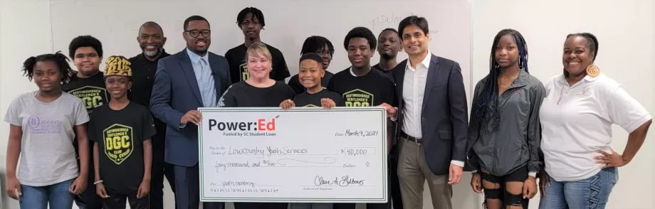 Students and adults pose with big ceremonial check in classroom