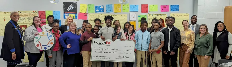 Students and adults pose with big ceremonial check in classroom