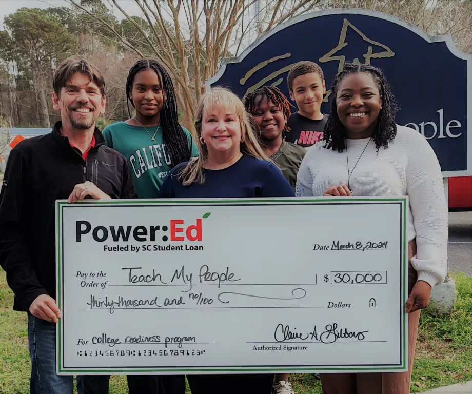 Two women, a man, and students pose with big ceremonial check.